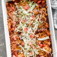 A pan of the best Cheese Enchiladas recipe, topped with shredded cabbage, chopped tomato, and cotija cheese.