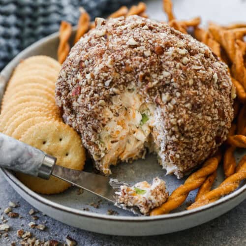 The best Cheese Ball with some cut and on a butter knife, served on a plate with crackers and pretzel sticks.