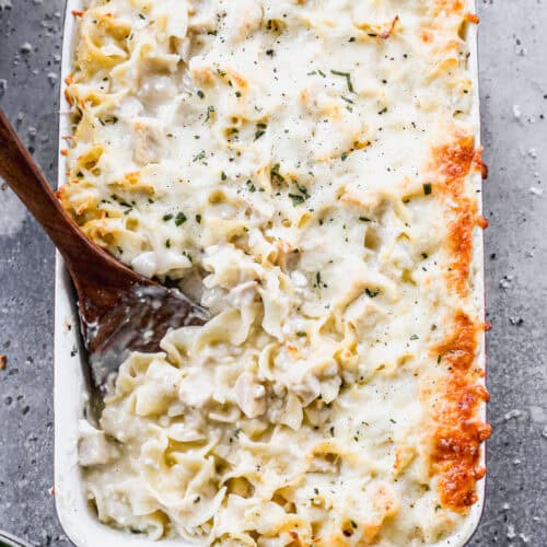 An easy Chicken Noodle Casserole recipe baked in a 9x13 pan with a wooden spoon scooping up a serving.