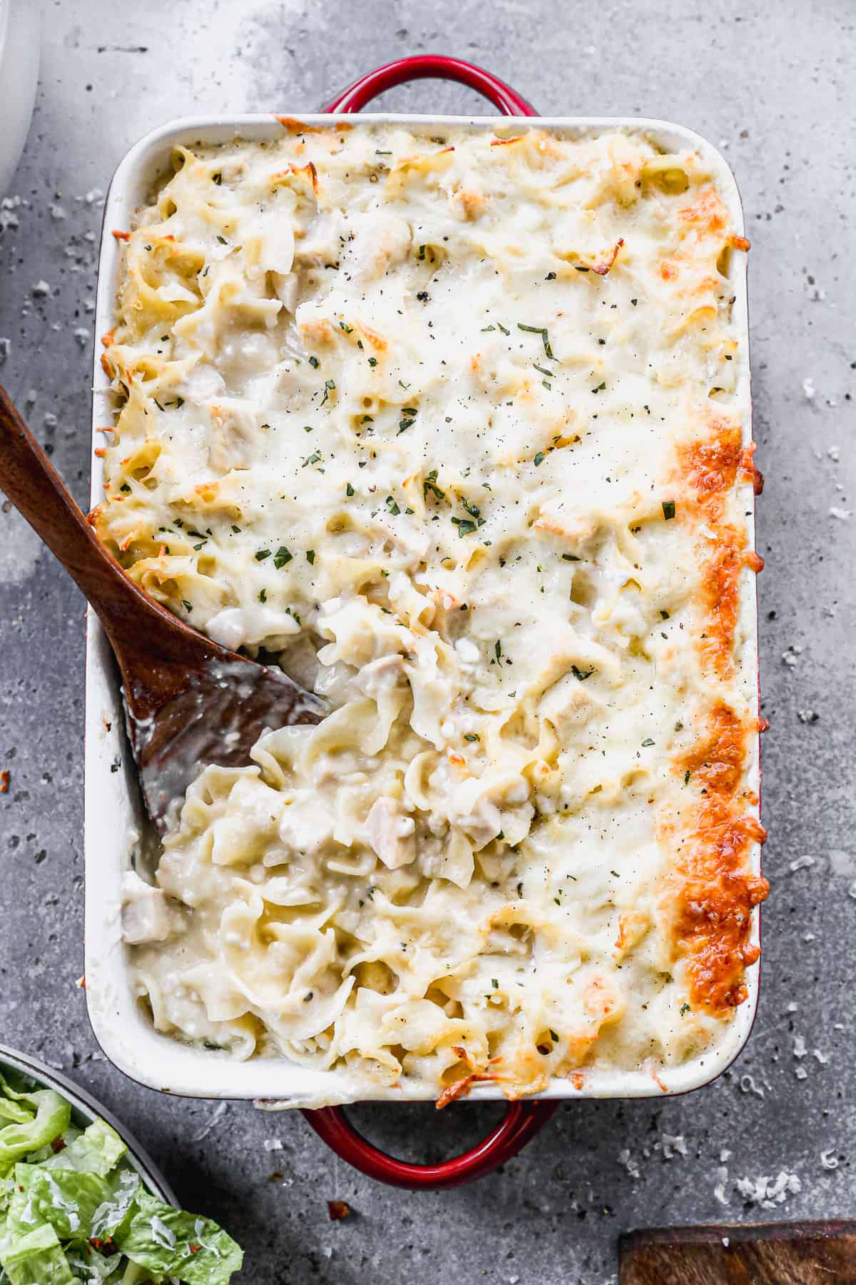 An easy Chicken Noodle Casserole recipe baked in a 9x13 pan with a wooden spoon scooping up a serving. 