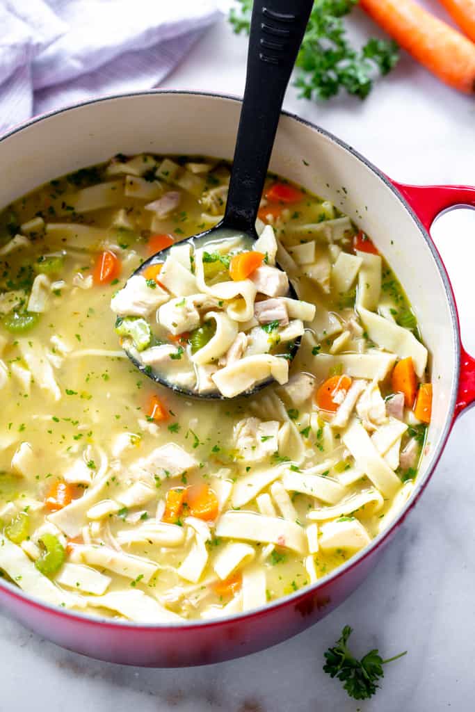 A ladle full of homemade chicken noodle soup lifting if from the soup pot.