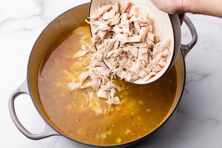 Rotisserie chicken being added to a large soup pot of chicken noodle soup.