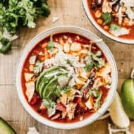 A bowl of homemade Chicken Tortilla Soup with crumbled tortilla soup, cheese, and sliced avocado.