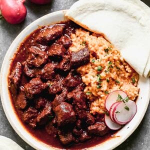 Chile Colorado served on a plate with Mexican rice and corn tortillas.