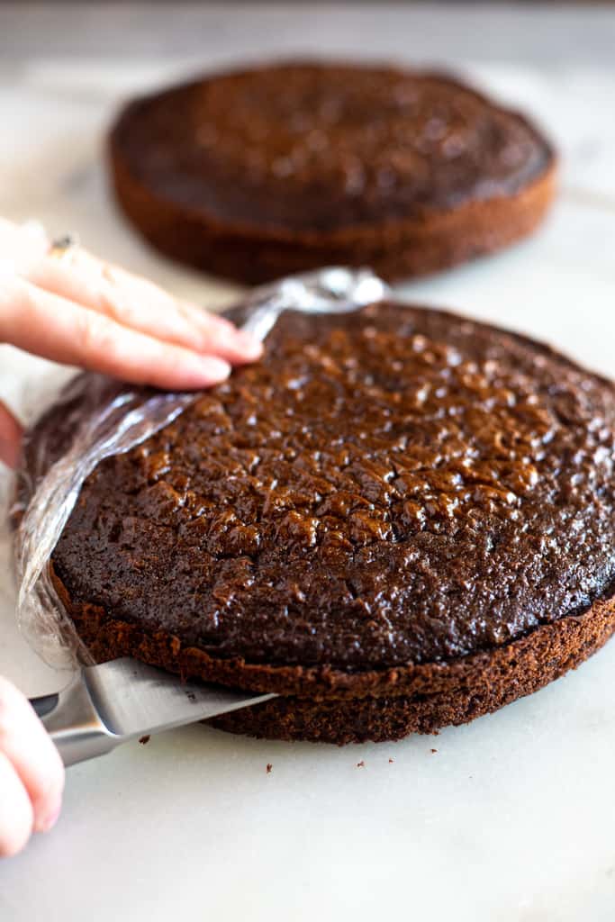 A baked chocolate cake round being cut in half, horizontally.