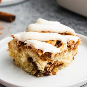 A slice of an easy Cinnamon Roll Cake recipe, topped with cream cheese frosting and served on a white plate.