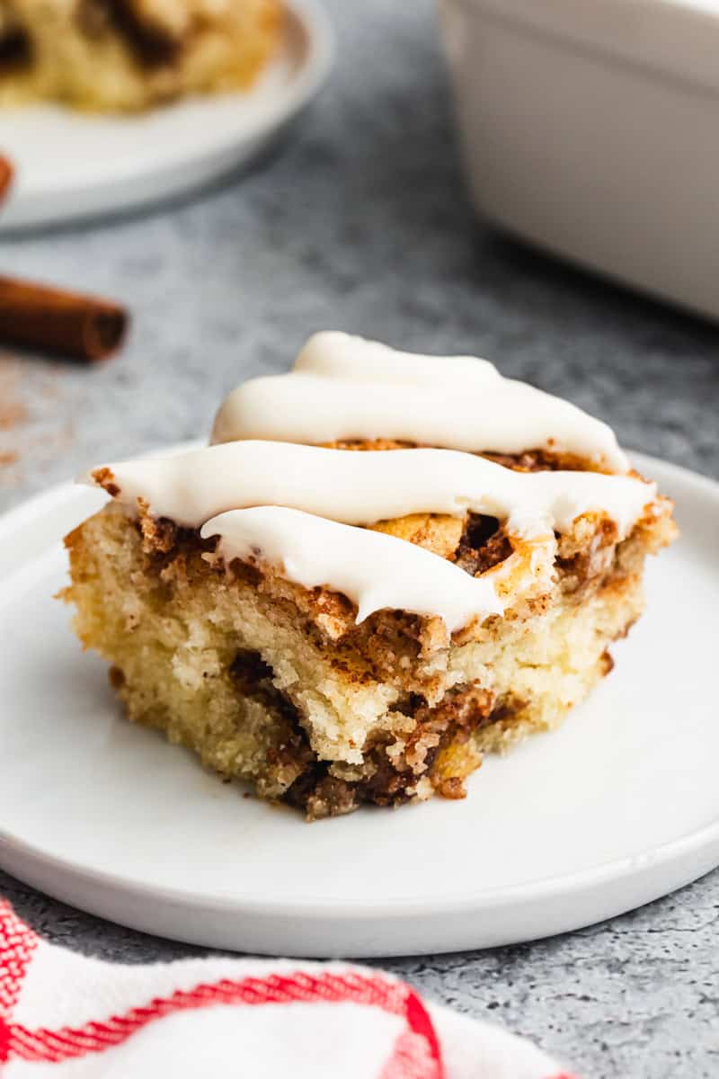 A slice of an easy Cinnamon Roll Cake recipe, topped with cream cheese frosting and served on a white plate. 