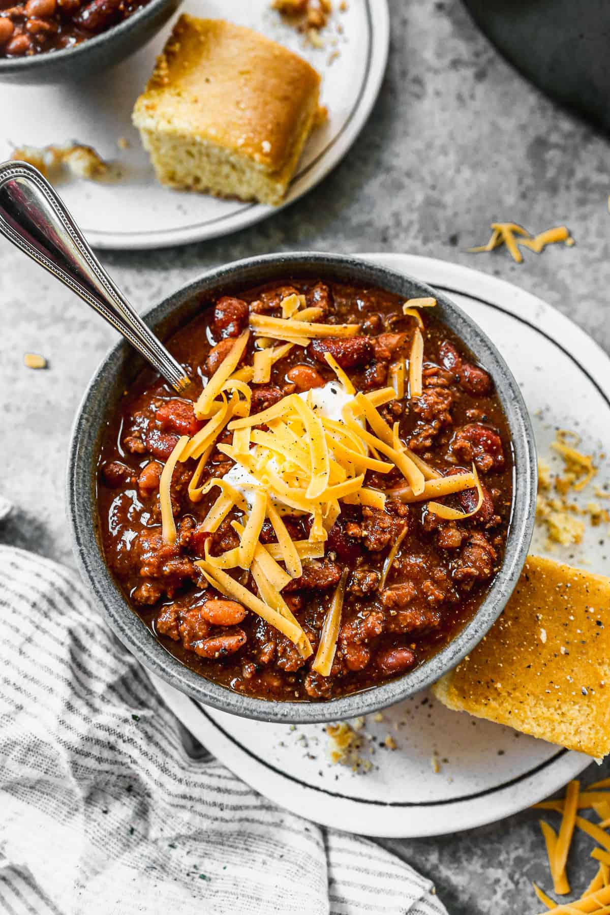 A bowl of the best classic chili recipe, topped with cheese and sour cream and a side of cornbread.