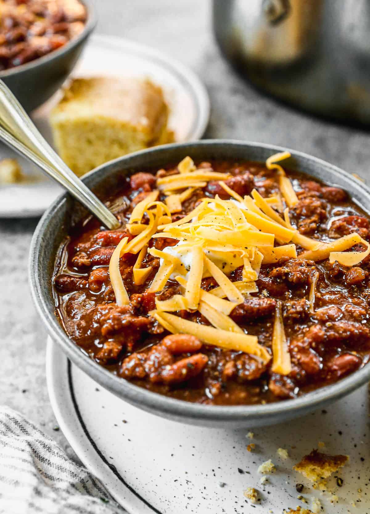 A bowl of homemade chili topped with a dollop of sour cream and some shredded cheddar cheese.