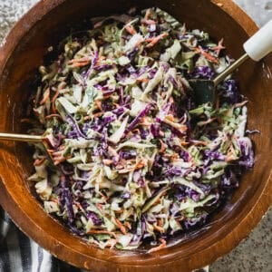 The best Coleslaw recipe with crunchy cabbage, green onions, carrots, and a creamy homemade dressing all tossed in a wooden bowl and ready to serve.