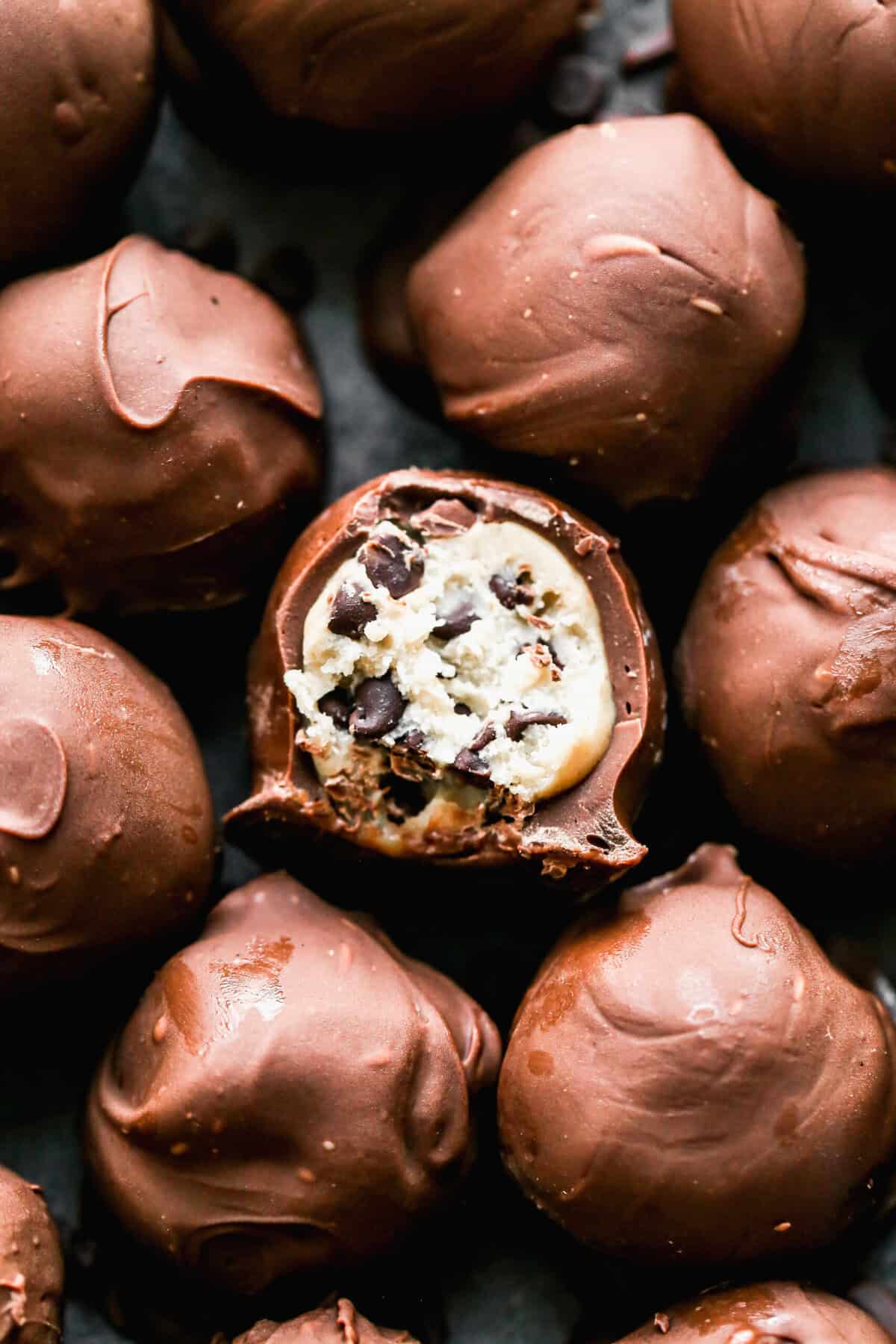 Chocolate Chip Cookie Dough Truffles in a pile with a bite out of the center one to show the cookie dough center. 