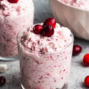 An easy Cranberry Fluff salad recipe served in a glass and topped with three fresh cranberries.