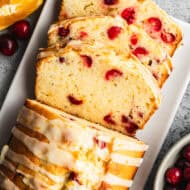 The best Cranberry Orange Bread recipe with an orange glaze, with three slices to show cut and served on a white tray.