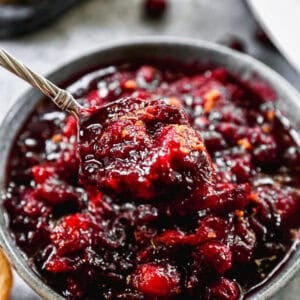 A cooked Cranberry Sauce recipe in a bowl with a spoon lifting some up.