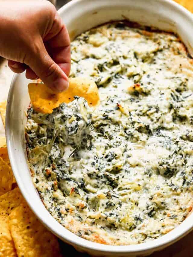 Spinach artichoke dip with a chip taking a scoop.