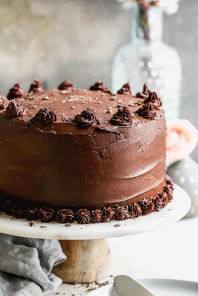 A serving platter with a three layer Dark Chocolate Cake on it.