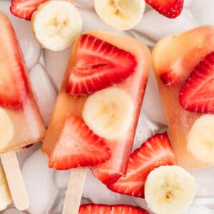 Homemade fruit popsicles made with sliced strawberries, bananas, and apple juice.