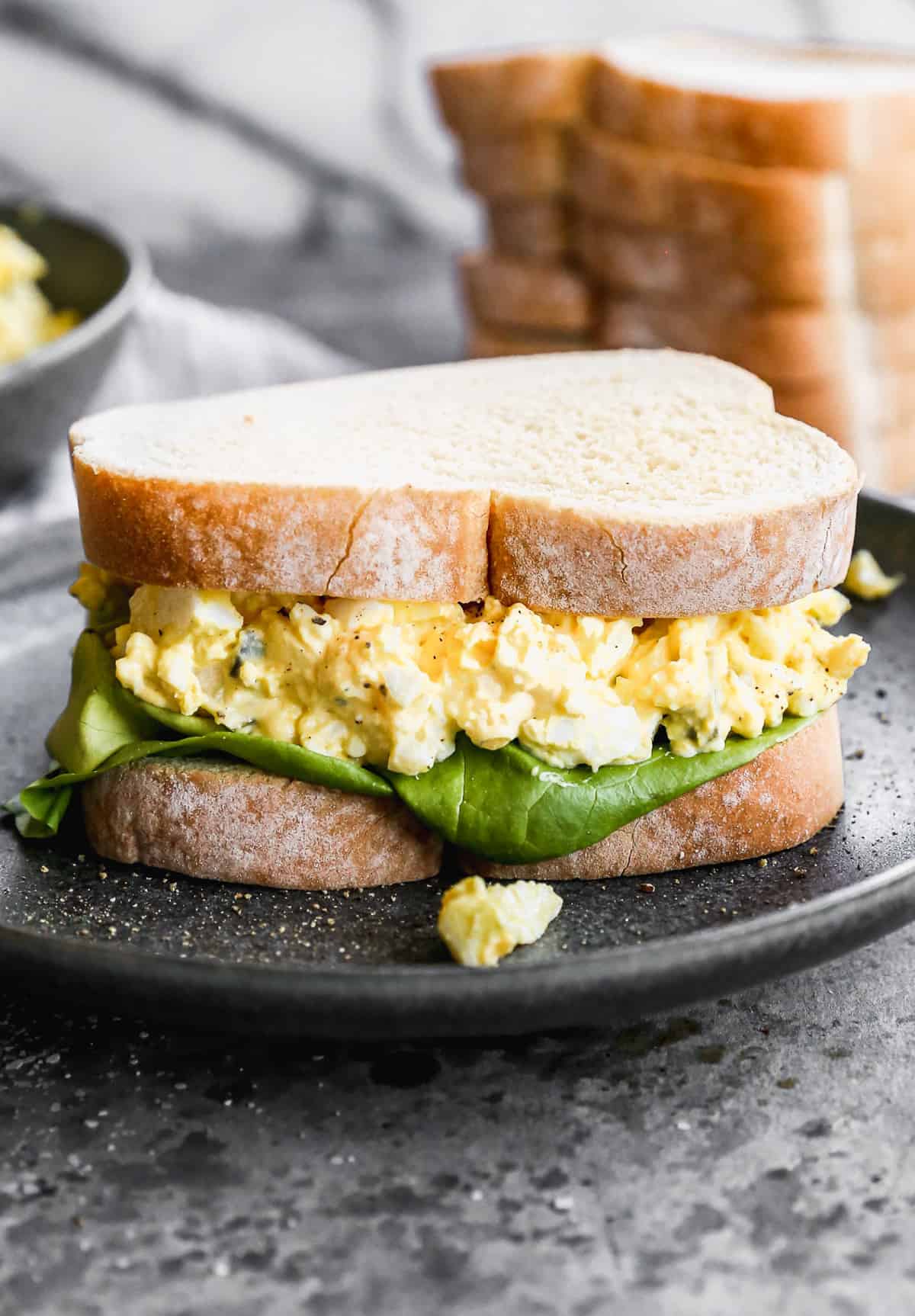 An egg salad sandwich on a black plate, ready to enjoy.