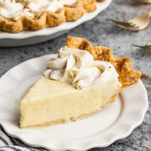 A slice of a no-bake eggnog pie recipe with whipped cream and cinnamon sprinkled on top. Served on a white plate, ready to eat.