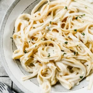 A bowl of the best fettuccine alfredo recipe topped with a sprinkle of fresh parsley and parmesan cheese.