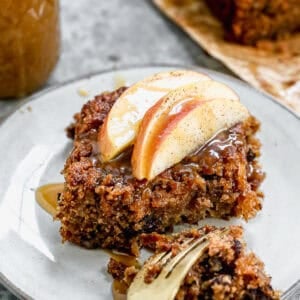 A piece of Fresh Apple Cake recipe on a plate, topped with a fresh sliced apple and a drizzle of homemade caramel sauce.