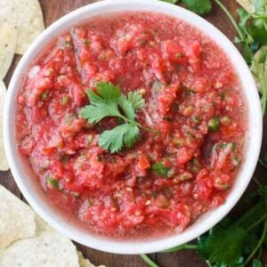 Fresh homemade salsa served in a white bowl made with roma tomatoes, cilantro, onion, serrano peppers, garlic and salt.