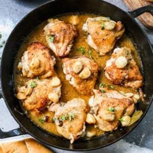 A creamy garlic chicken recipe made with chicken thighs and 40 cloves of garlic in a cast iron pan, ready to serve.