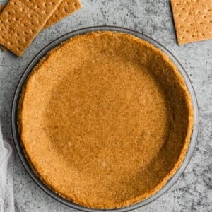 A homemade graham cracker crust inside a glass pie plate with scattered graham crackers around it.