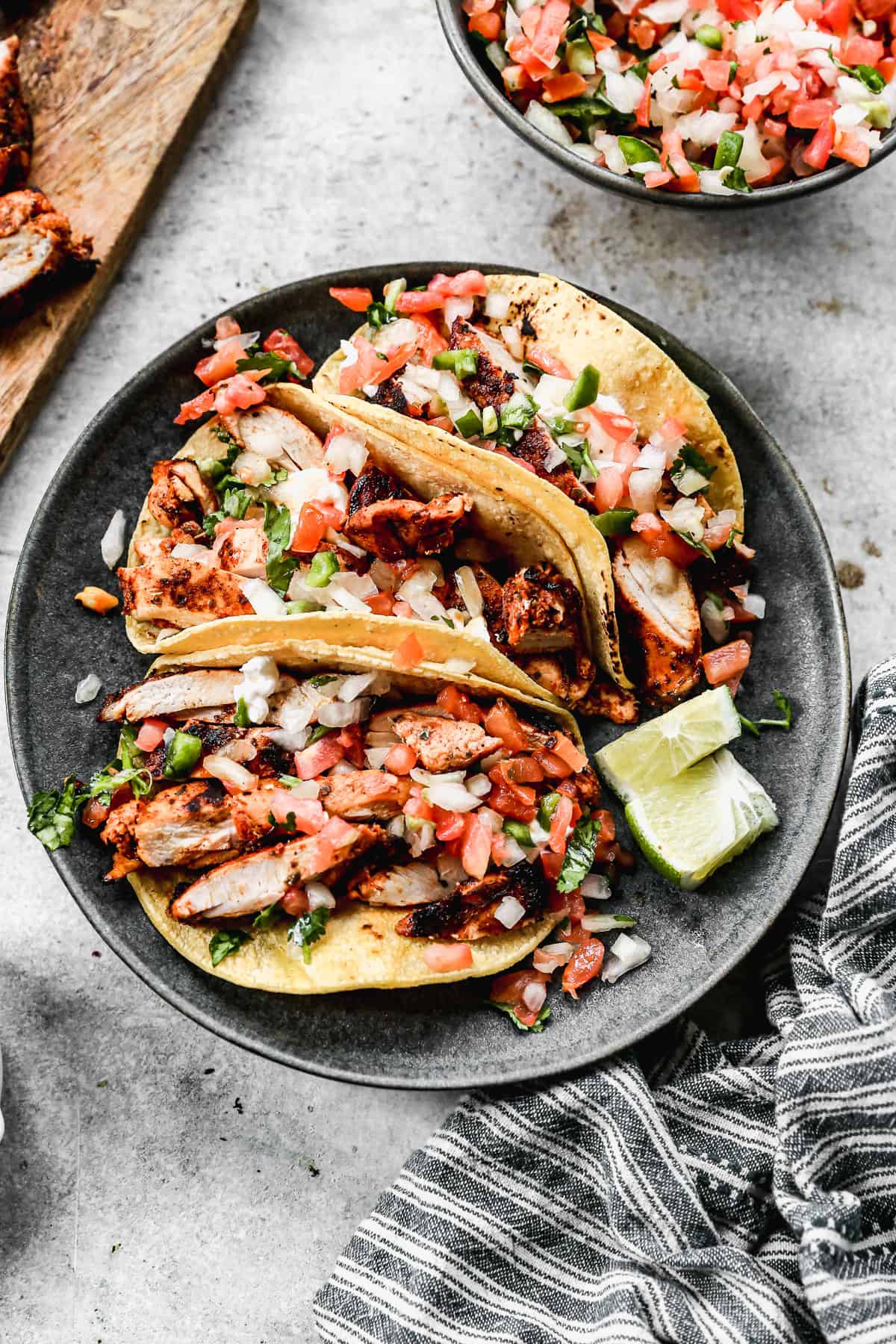 Three Chicken Street Tacos on a plate topped with fresh pico de gallo and cilantro and a couple lime wedges on the side.