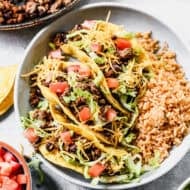 The best ground beef taco recipe with fresh fried tortillas topped with lettuce, tomatoes, with a side of Mexican rice.