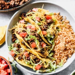 The best ground beef taco recipe with fresh fried tortillas topped with lettuce, tomatoes, with a side of Mexican rice.