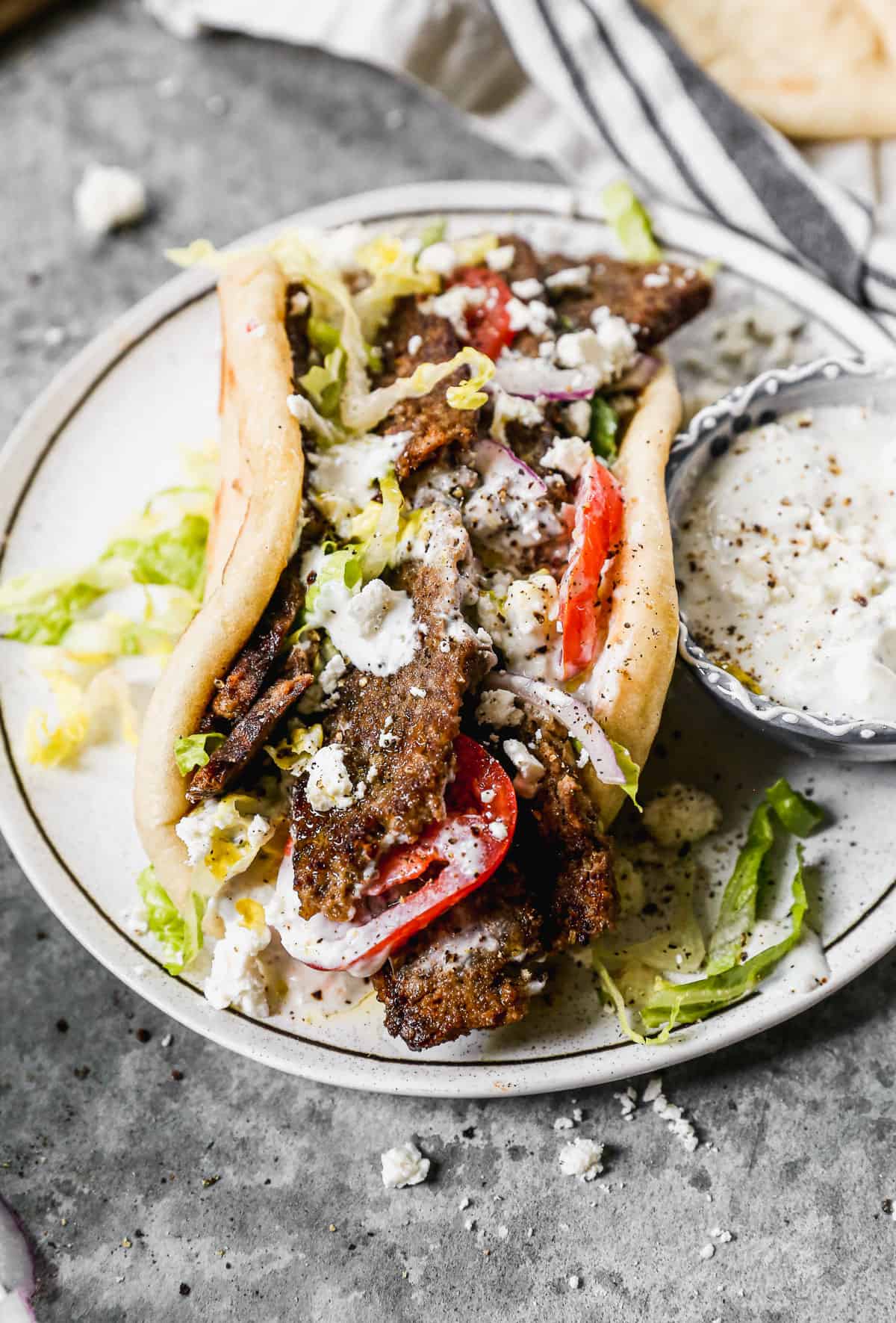 A homemade gyro including gyro meat served in a pita with lettuce, tomato, red onion, and tzatziki sauce.