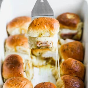 A pan of a Ham and Cheese Sliders recipe with one being lifted to show the melted cheese.