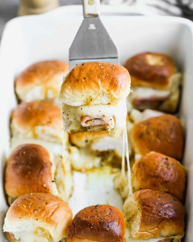 A pan of a Ham and Cheese Sliders recipe with one being lifted to show the melted cheese. 