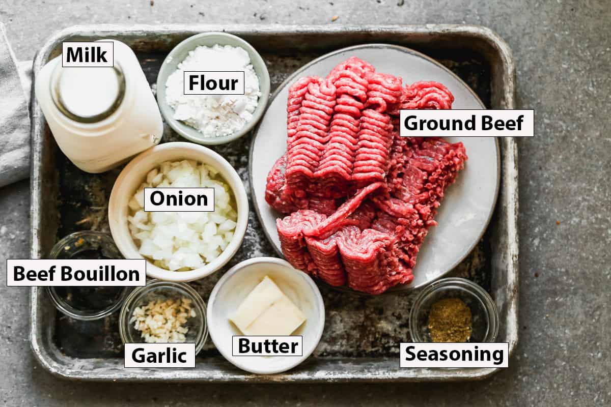 The ingredients needed to make hamburger gravy, including ground beef, onion, flour, milk, butter and spices.