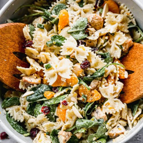 A cold Chicken Pasta Salad recipe in a big bowl with wooden tongs starting to pick some up.