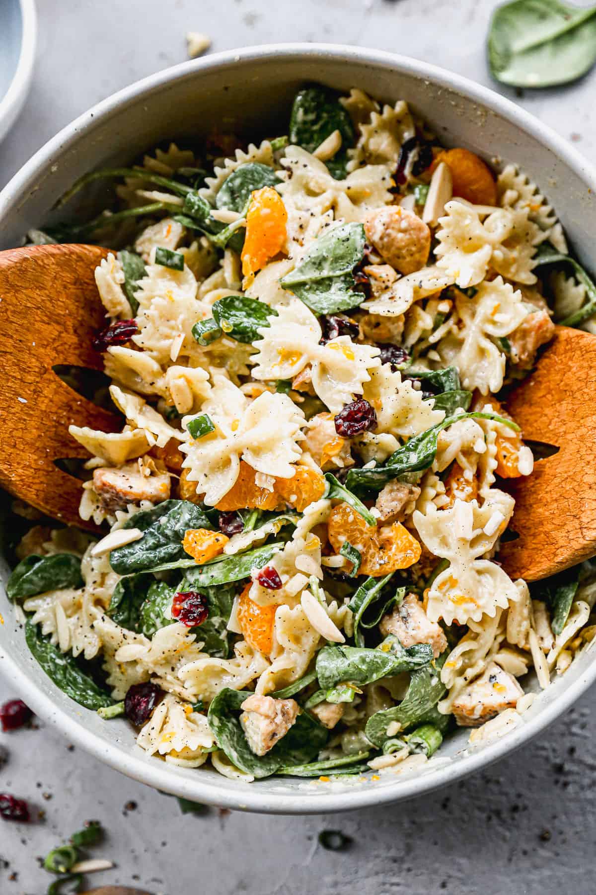 A cold Chicken Pasta Salad recipe in a big bowl with wooden tongs starting to pick some up. 