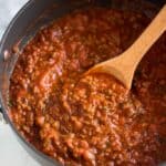 Homemade spaghetti sauce in a saucepan with a wooden spoon.