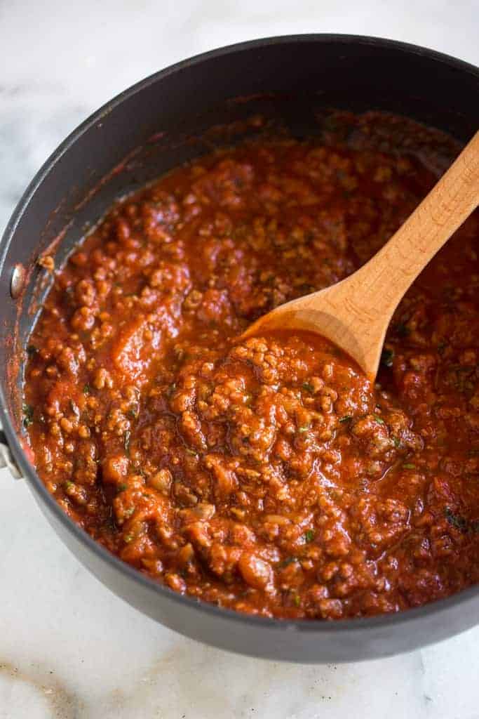 Homemade spaghetti sauce in a saucepan with a wooden spoon.