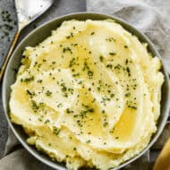 A bowl of Instant Pot Mashed potatoes drizzled with melted butter and chives, ready to serve.