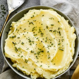 A bowl of Instant Pot Mashed potatoes drizzled with melted butter and chives, ready to serve.