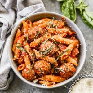 A bowl of Instant Pot Pasta and Meatballs topped with grated parmesan cheese and strips of basil, ready to enjoy.