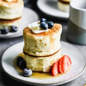 Two Japanese souffle pancakes stacked on top of each other topped with butter, maple syrup, and some fresh berries.