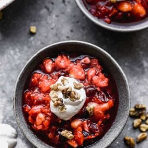 A bowl of Jello fruit salad with whipped cream and nuts on top.