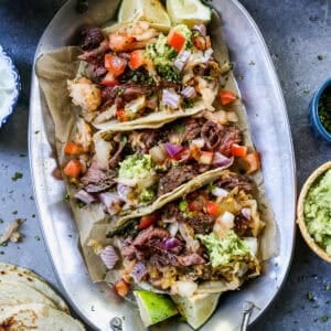 Three Korean Beef Tacos on a platter topped with kimchi salsa, guacamole, and cilantro.