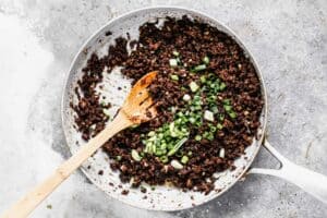 Chopped green onion added on top of Korean ground beef cooking in a skillet.