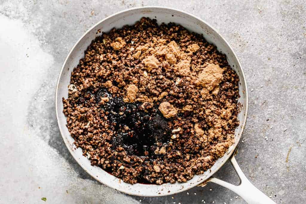 Crumbled ground beef in a skillet with spice and seasonings added on top.