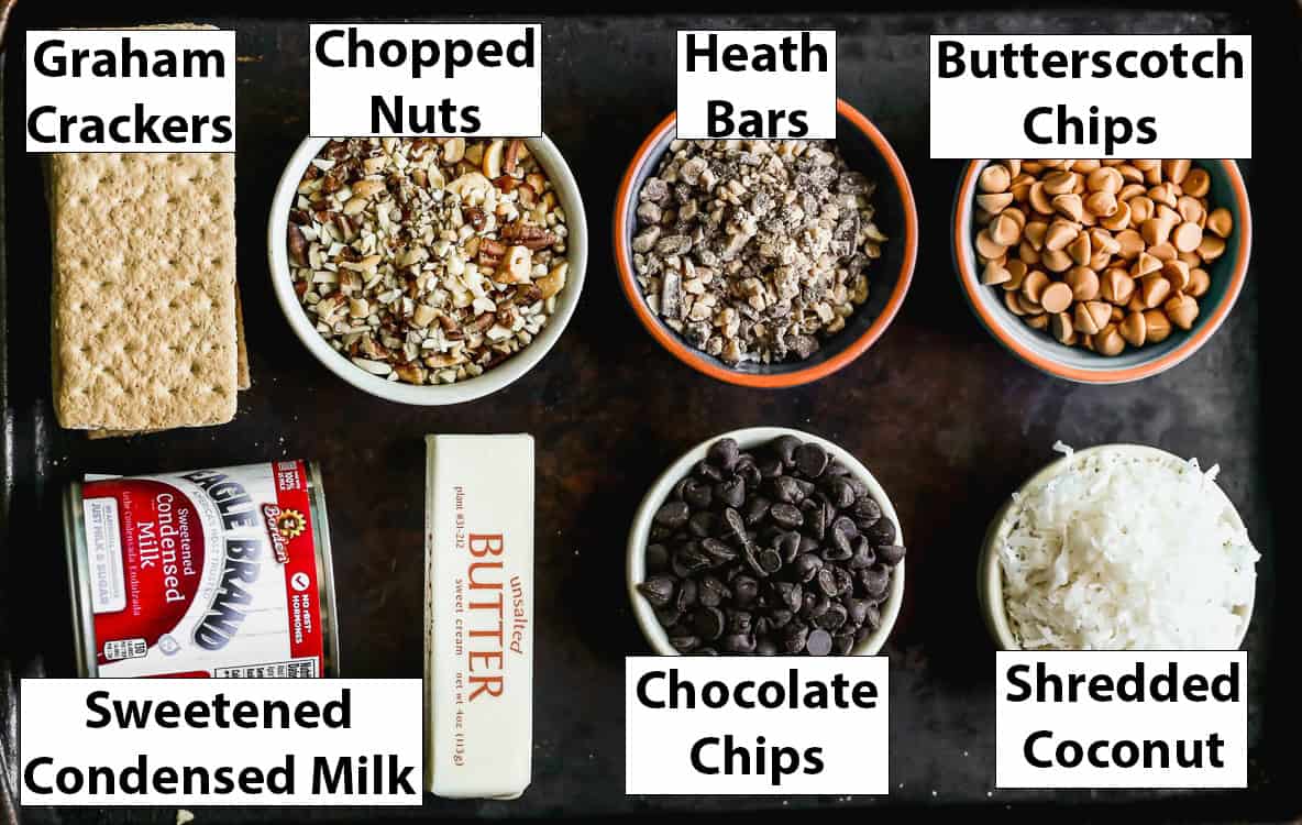 All of the ingredients for 7 Layer Bars: graham crackers, nuts, heath bars, butterscotch chips, sweetened condensed milk, chocolate chips, and shredded coconut. 