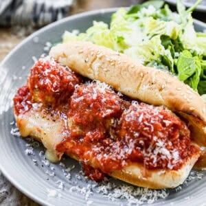 A homemade Meatball Sub sandwich recipe with a toasted sub with melted cheese, topped with three meatballs, marinara sauce, and a sprinkle of parmesan cheese.