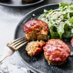 The best mini meatloaf recipe cooked in a muffin tin and topped with a flavorful sauce, served on a plate with a green salad.